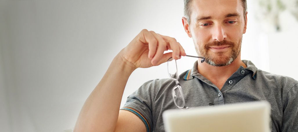 Man holding eye glasses looking at a tablet.